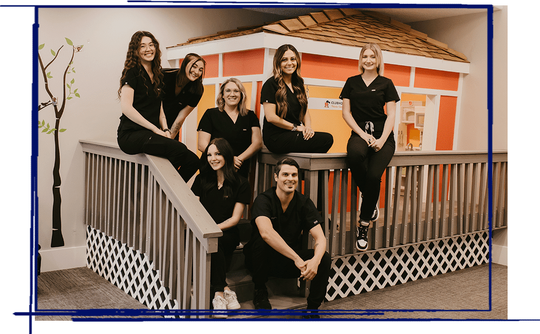 Team of dental professionals in black scrubs posed together on stairs in modern dental office.