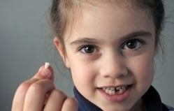 Young child smiling at camera with finger pointing, displaying healthy teeth in studio setting.
