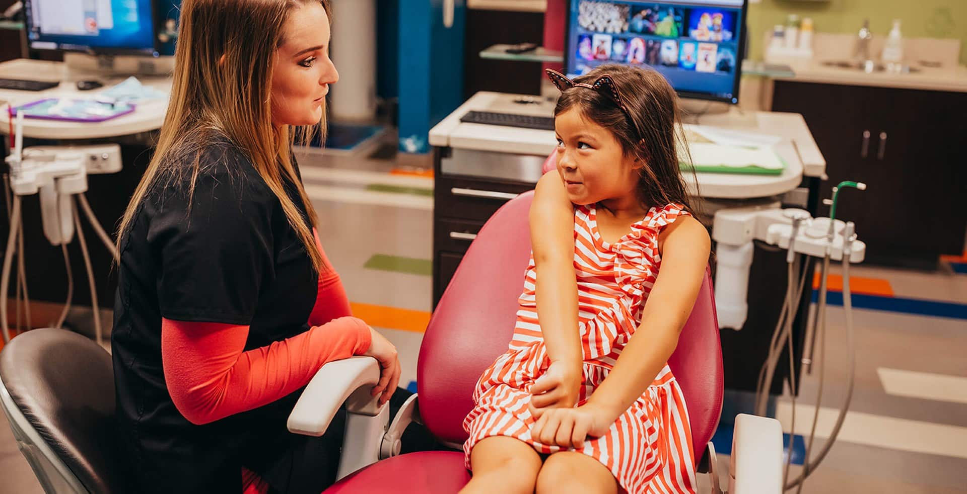Two women conversing in a pediatric dental office with computers visible in the background.