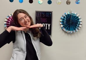 Female pediatric dentist posing playfully in dental office with colorful wall decorations and clocks.
