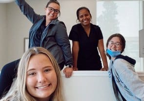 Pediatric dental team of four smiling professionals posing together in bright office setting.