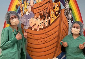 Two children in green shirts pose in front of colorful Noah's Ark mural at pediatric dental office.