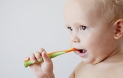 Toddler chewing on green teething toy against white background.