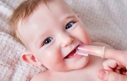 Happy toddler with teething toy in mouth, smiling on soft blanket background.
