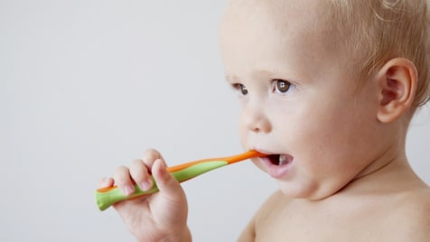 Toddler chewing on colorful toy teething ring against white background.