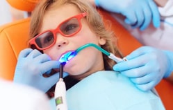 Child wearing protective eyewear receives dental treatment from dentist in clinical setting.