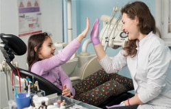 Pediatric dentist high-fiving young patient in dental chair during checkup visit.